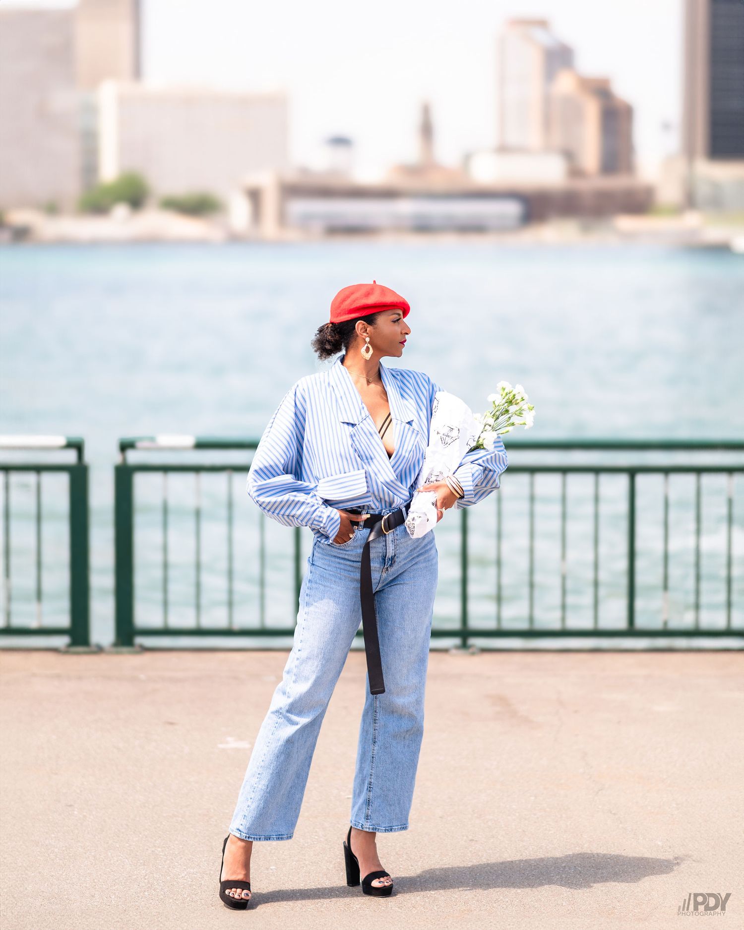 Fashion shoot at waterfront with blue outfit and red beret near ships and railing.