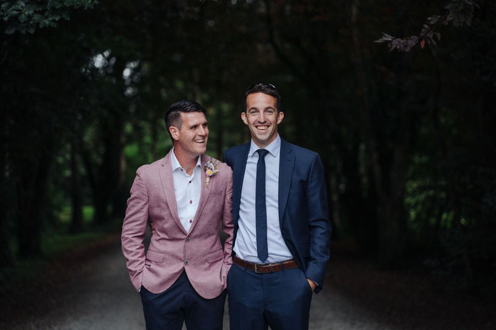 Two people in formal attire share a candid moment on a tree-lined path.