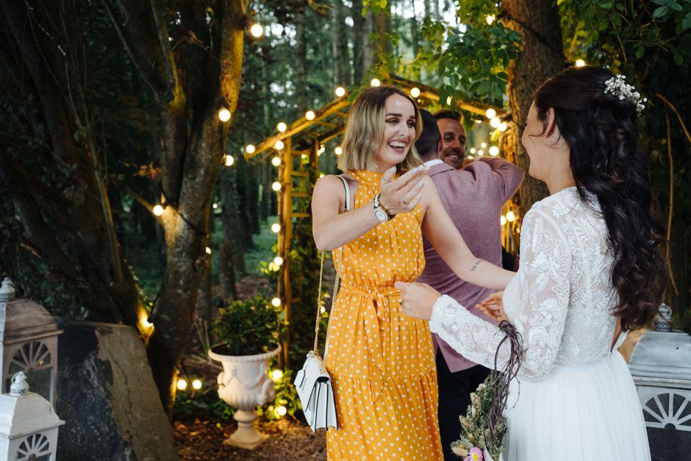 Wedding guests mingle under string lights at an outdoor forest reception.