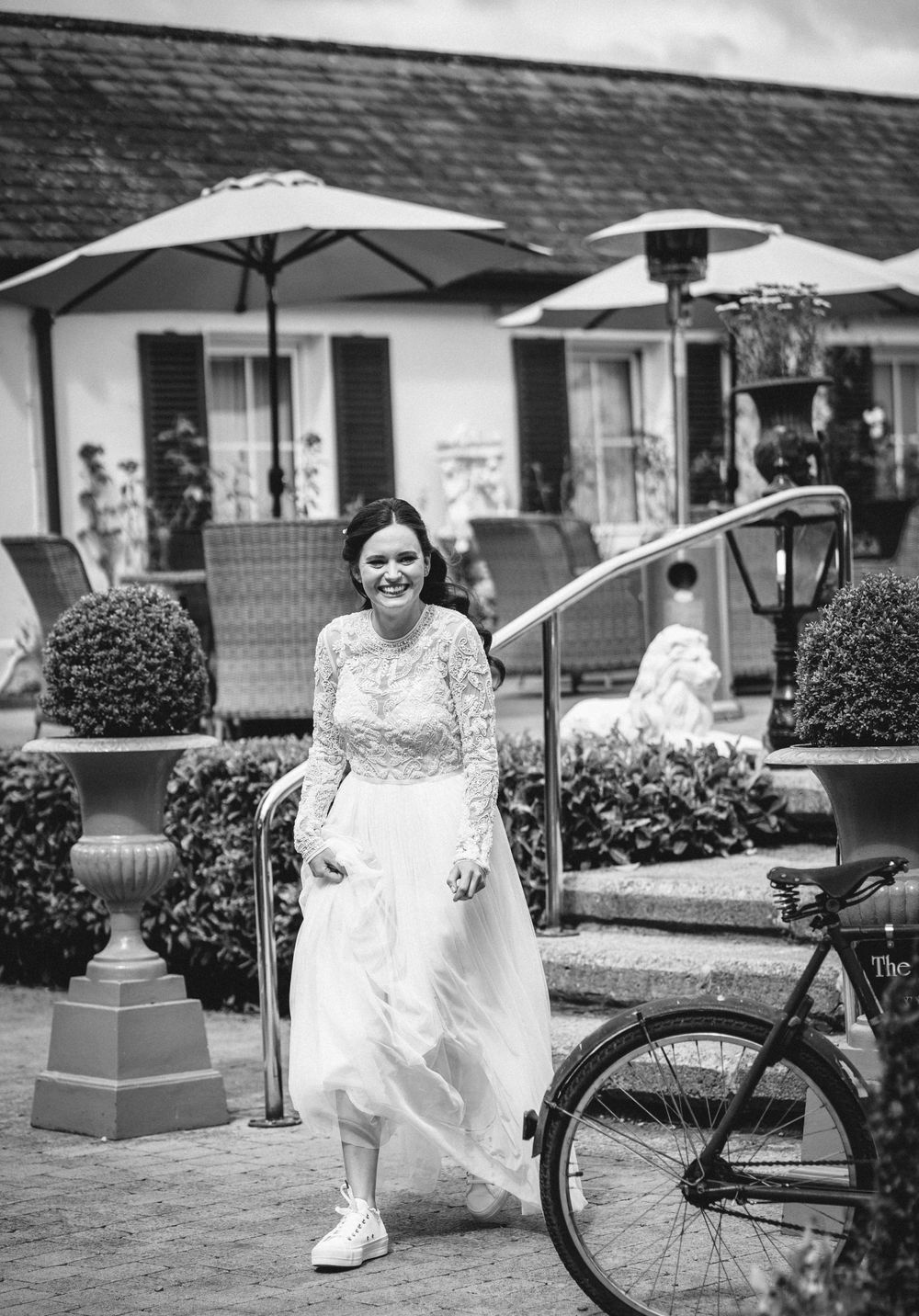 A wedding portrait with sneakers featuring a white dress and bicycle against ornate garden decor.