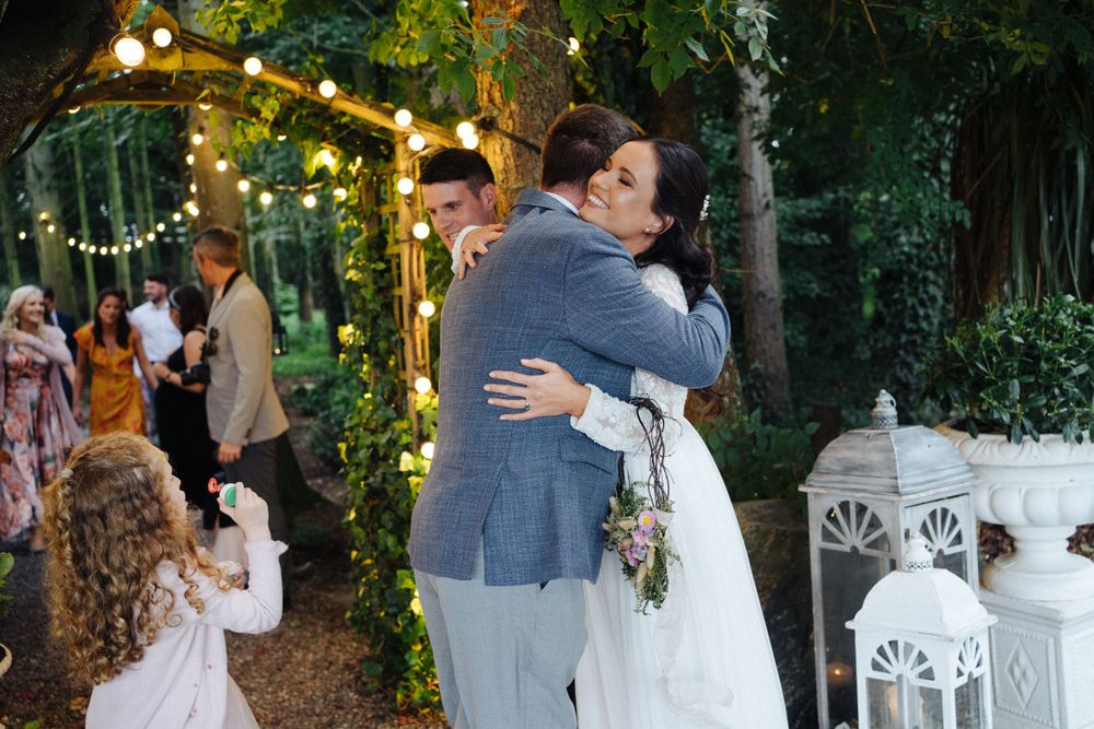 An emotional embrace during a wedding celebration in a garden setting with string lights.