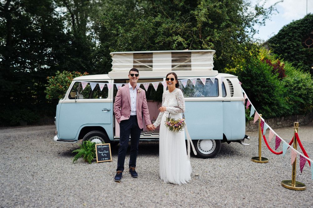 Rustic outdoor wedding scene with light blue vintage VW van and decorative bunting.