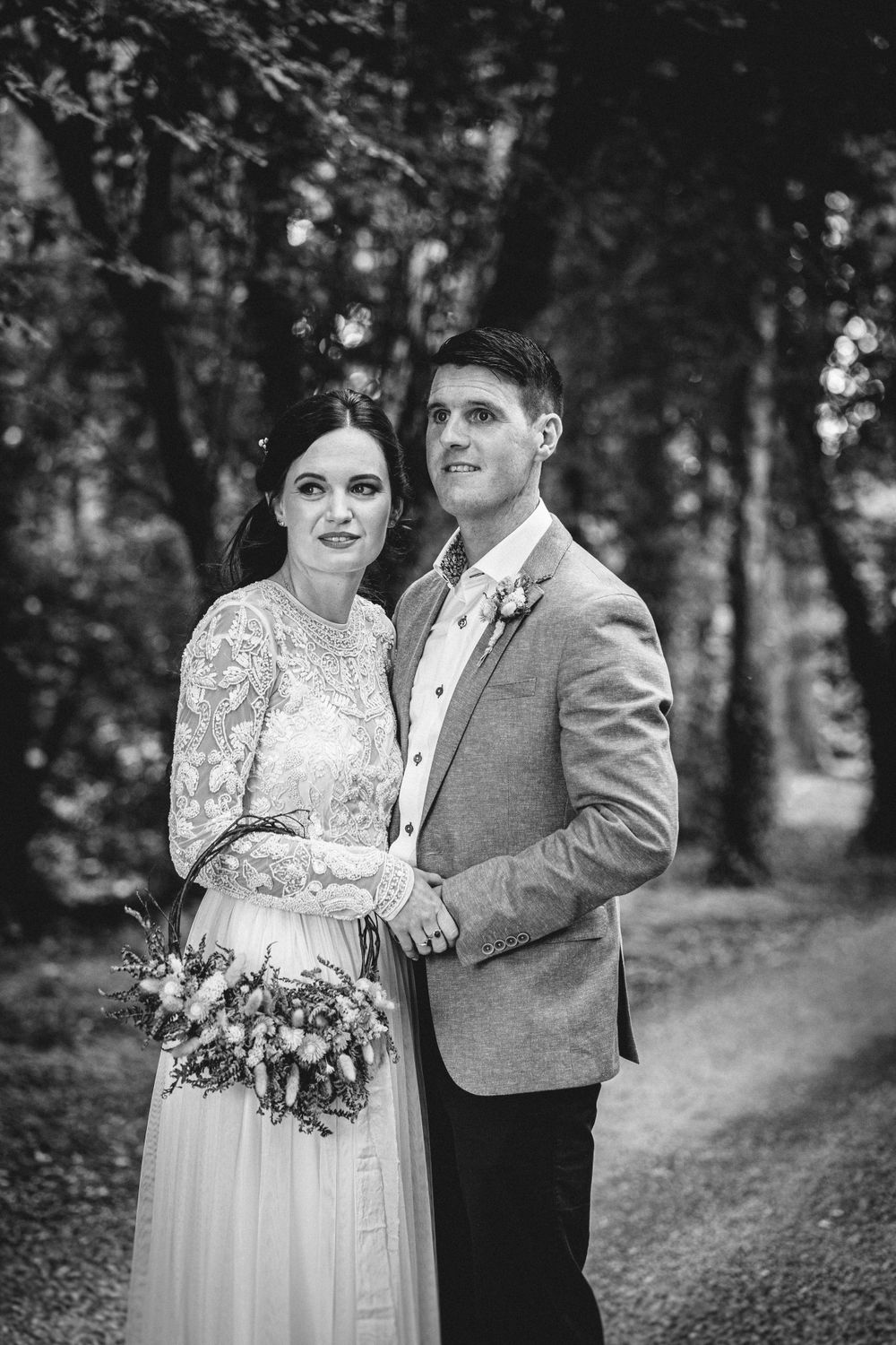 Black and white wedding portrait of a couple on a wooded path with rustic charm.