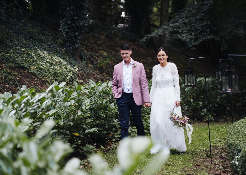 A wedding couple walking through a garden landscape with greenery and natural scenery.