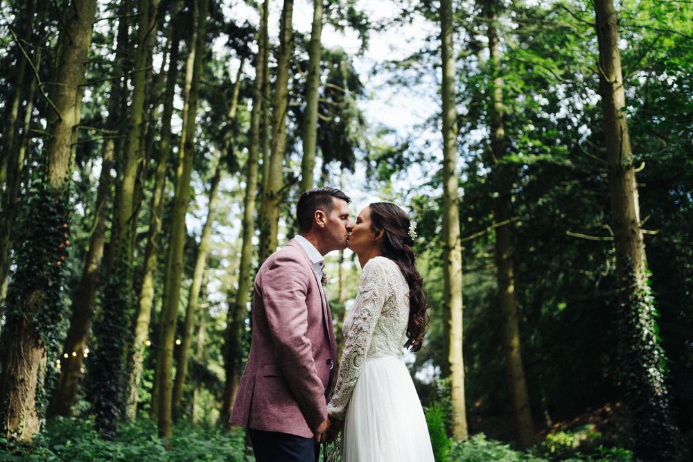 Intimate wedding moment captured in a forest setting with tall trees and natural lighting.