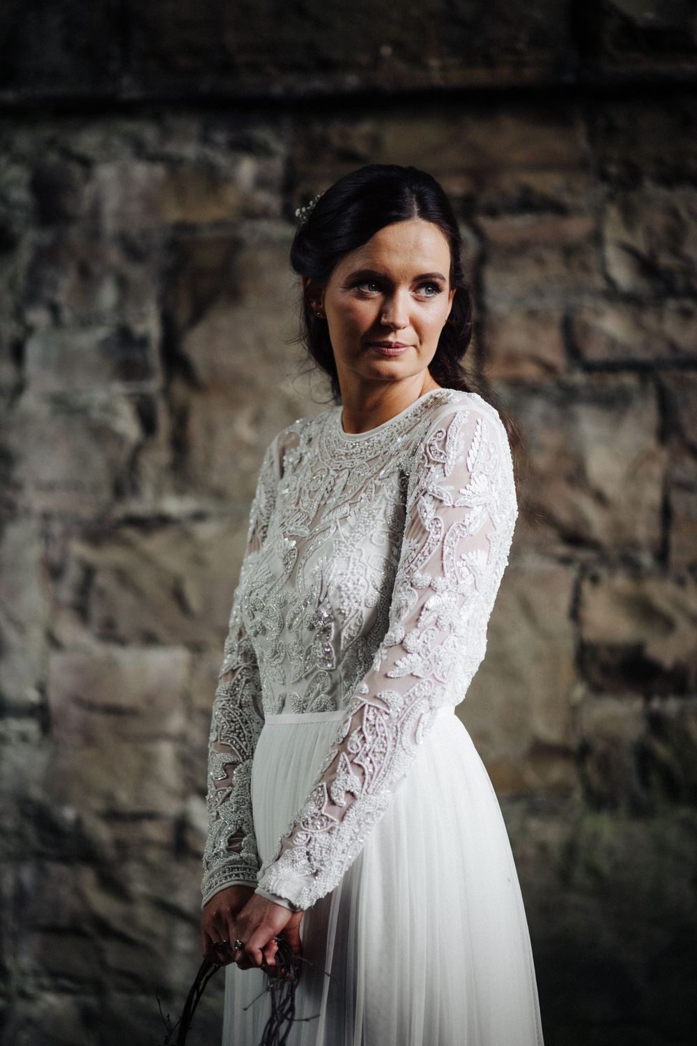Elegant bridal portrait against a stone wall featuring a long-sleeve lace wedding dress.