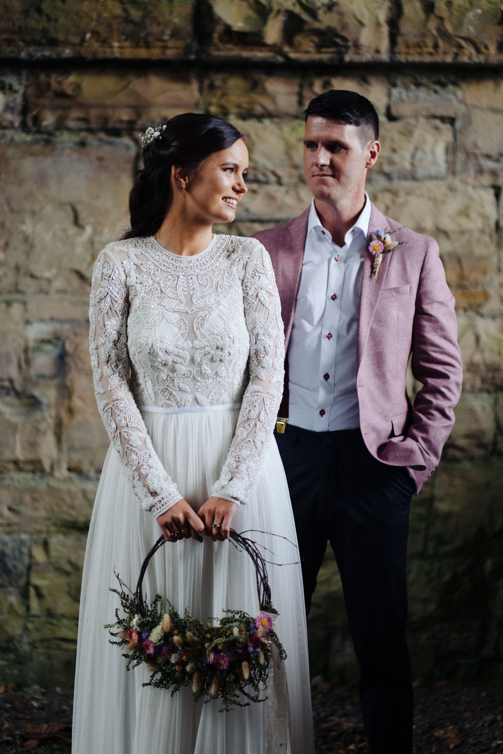 Stylish wedding portrait against stone wall backdrop with vintage-inspired bridal accessories.