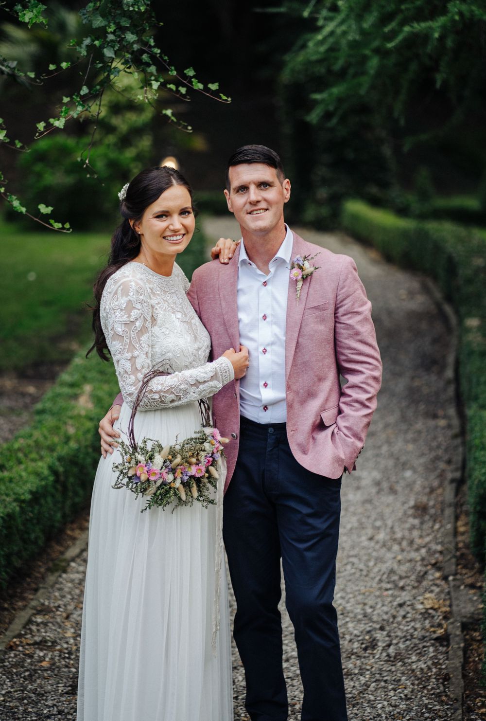Wedding couple posing on a garden path with the bride holding a rustic floral bouquet.