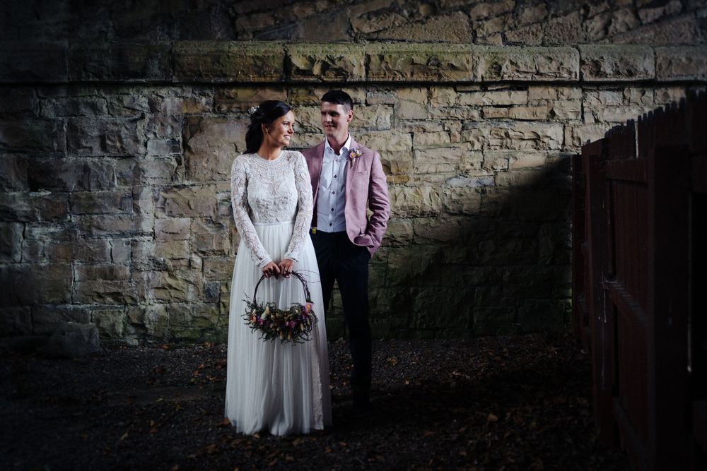 Dramatic wedding photo against stone wall with moody lighting and rustic decor.