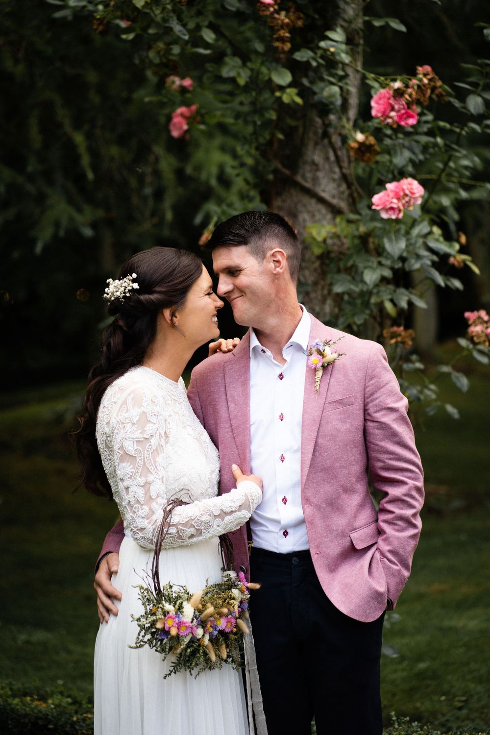 A romantic wedding portrait in a garden with pink roses as a couple shares an intimate moment.