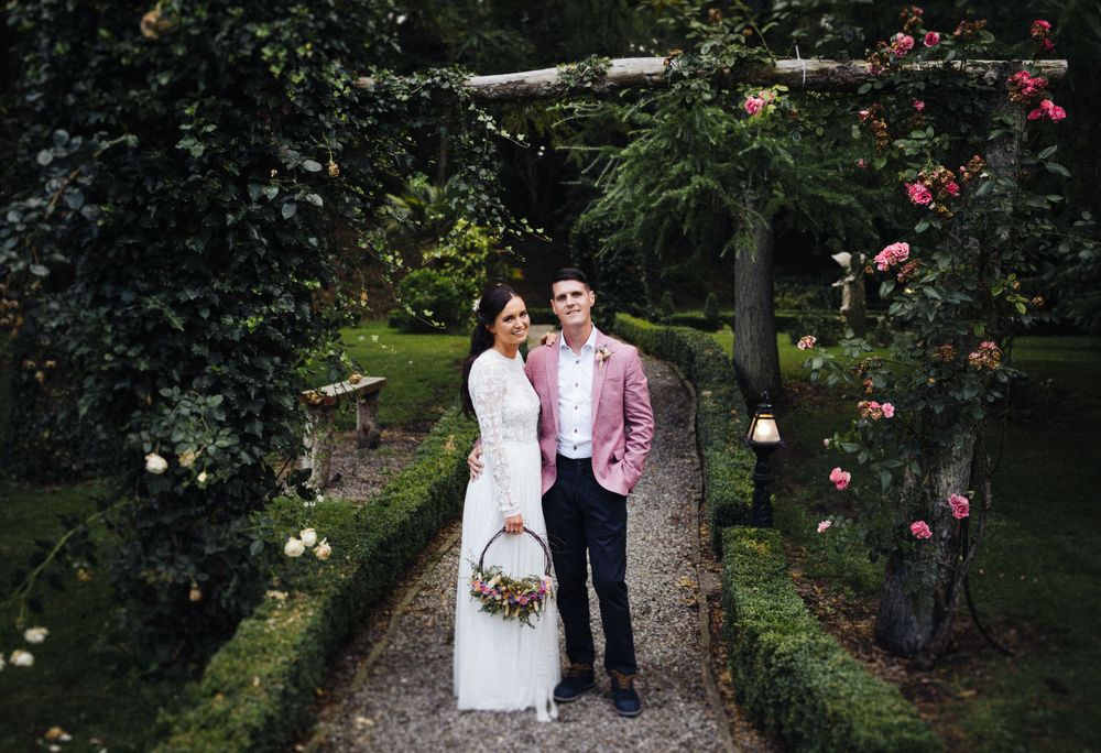Garden wedding portrait with climbing roses and a pink blazer adding a pop of color.