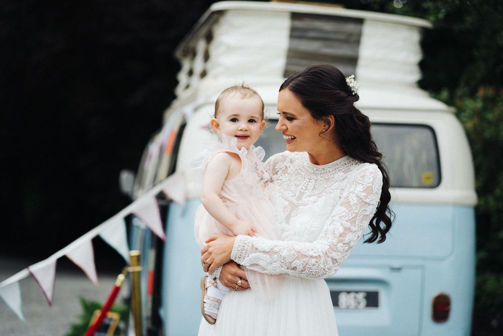 Sweet moment between a bride in lace and a small child with vintage blue van in background.