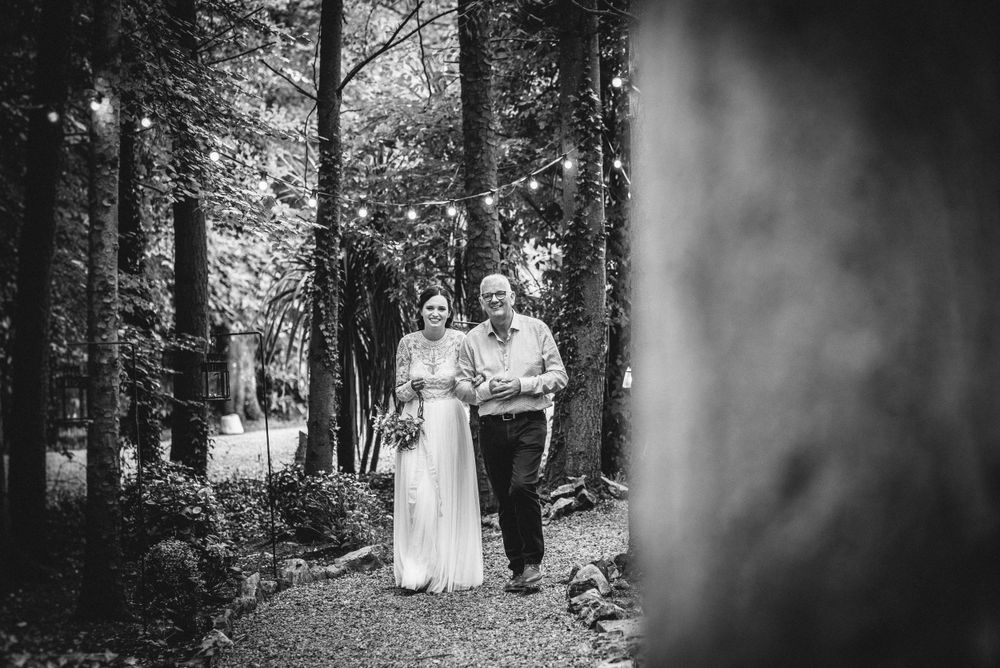 Black and white photo of two people walking together on a wooded path.