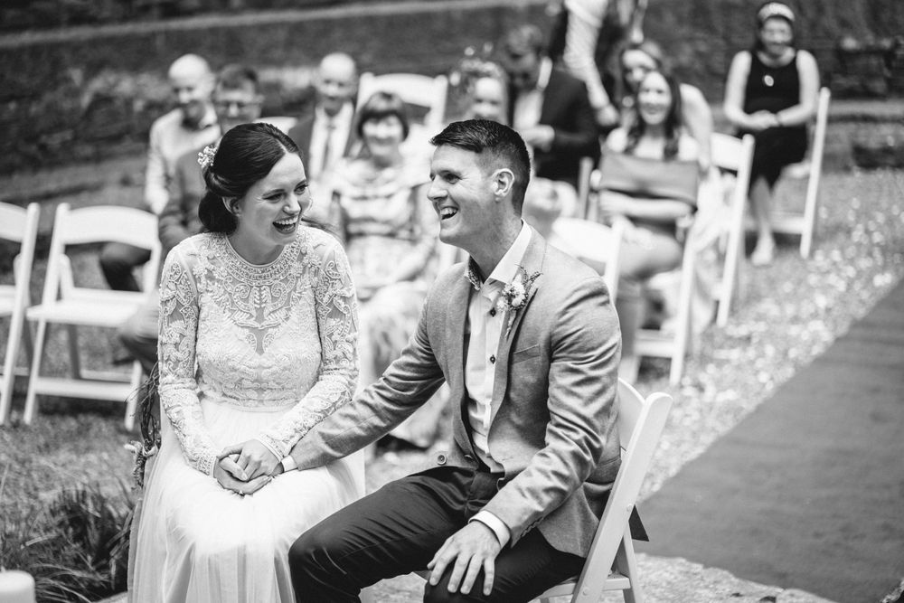 Wedding ceremony candid moment with guests seated on white chairs in the background.