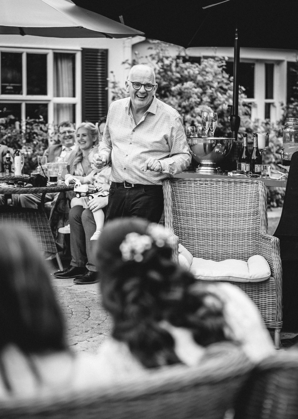A speaker addresses guests at an outdoor garden party in black and white.