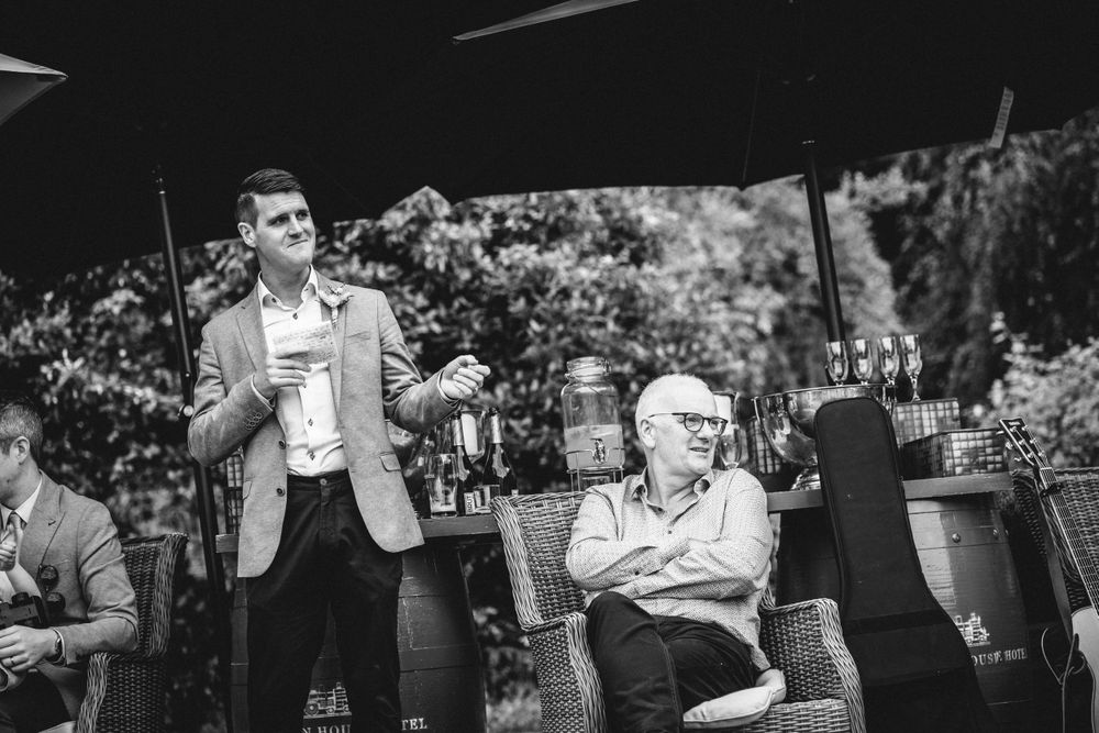 Black and white photo of guests talking during an outdoor garden reception with seating.