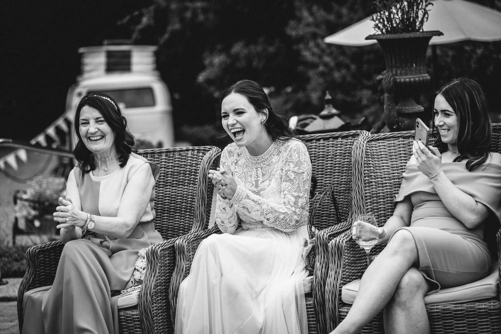 Black and white image showing three people laughing while seated on outdoor wicker furniture.