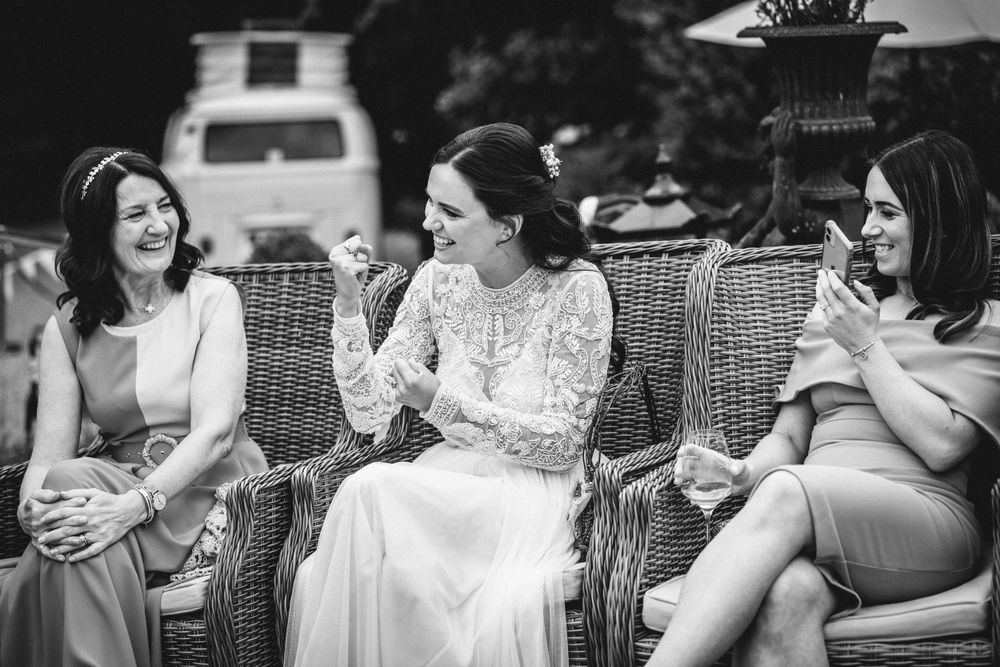 Three guests share a candid moment while seated on wicker furniture at an outdoor event.