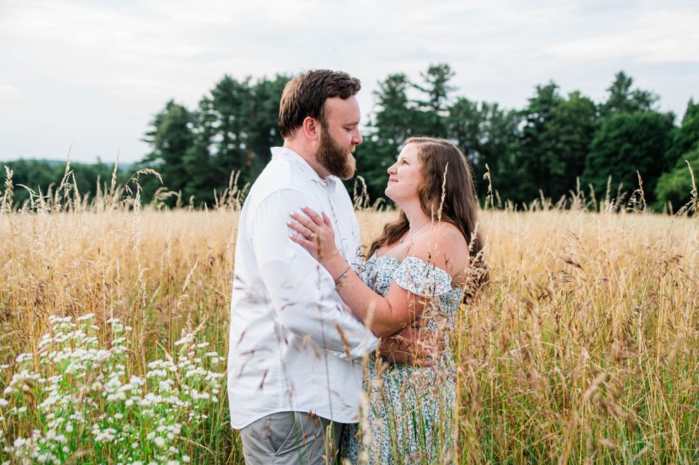 A couple embraces in a sunny field of tall grass during an engagement photoshoot.