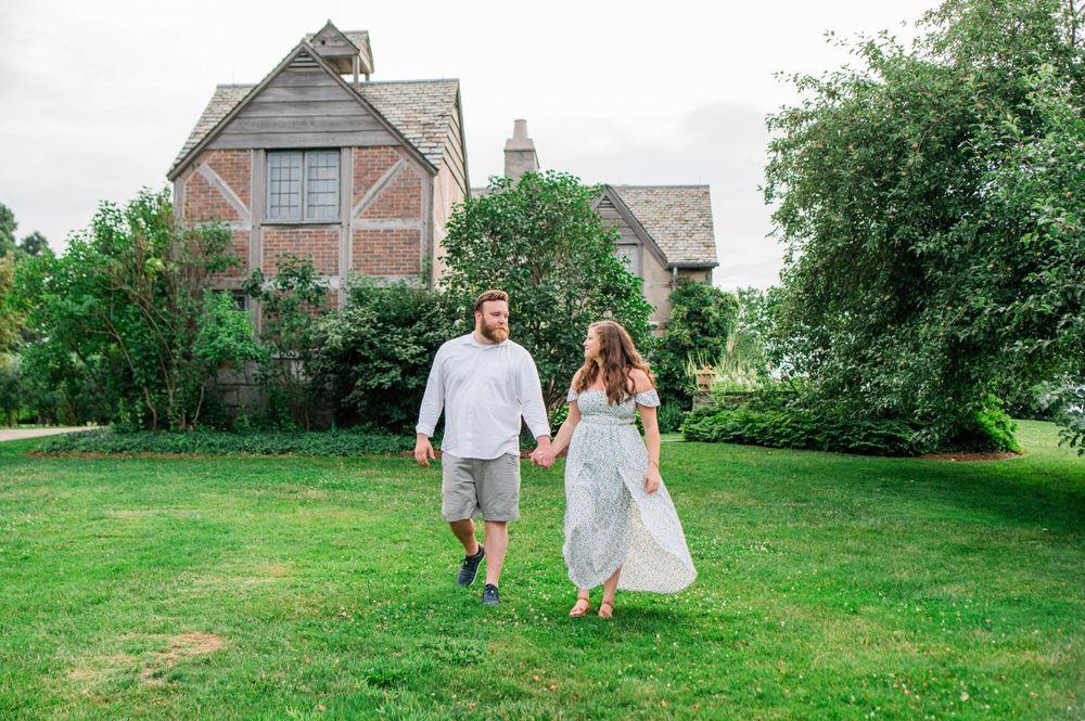 A couple strolling through a beautiful garden with Tudor-style houses in the background.