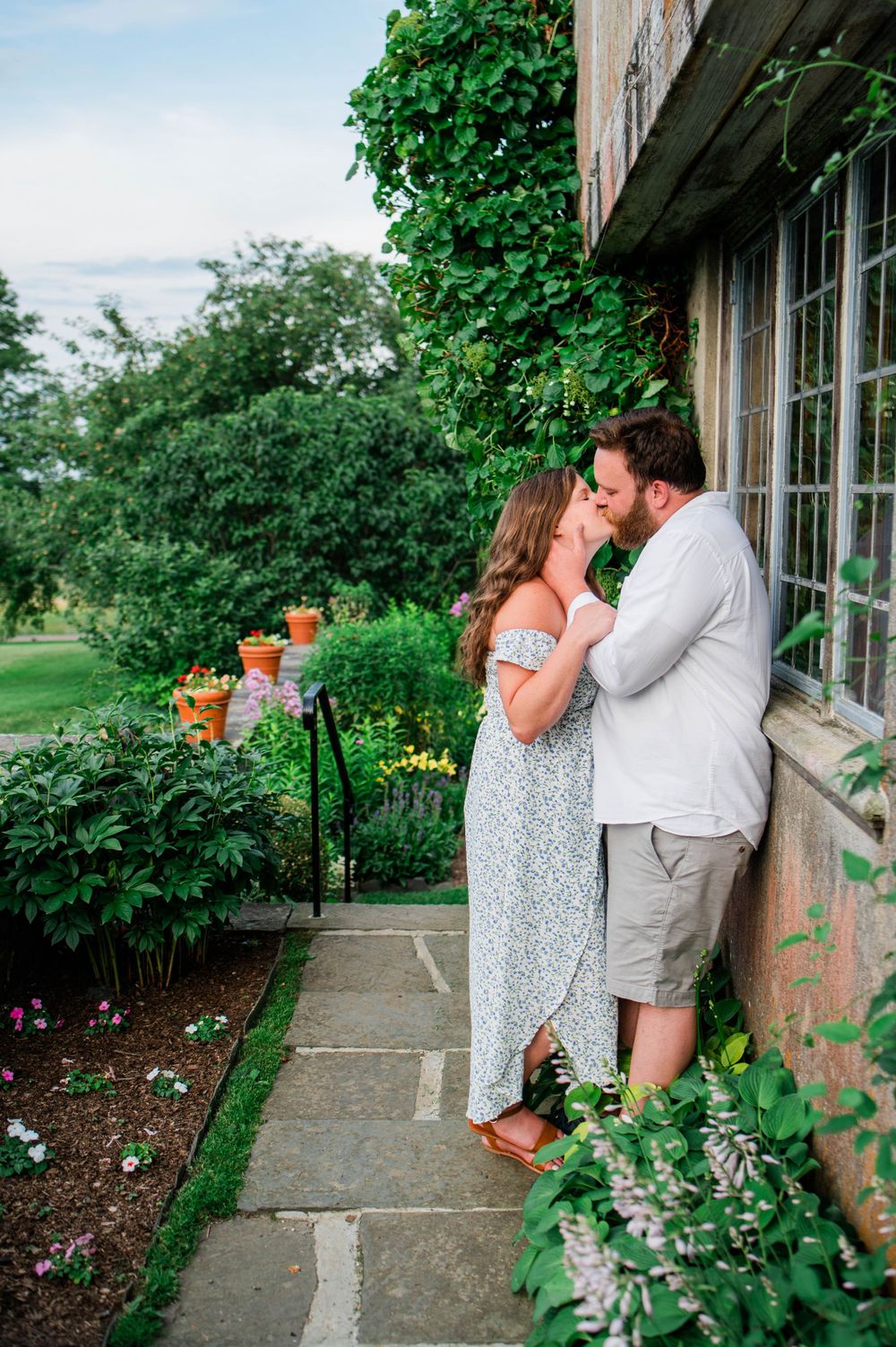 A tender moment shared beside a stone building surrounded by colorful garden flowers and climbing vines.