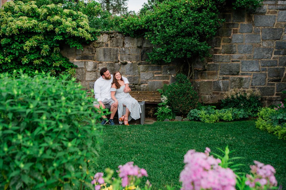 A romantic scene on a garden bench surrounded by lush greenery and blooming pink flowers.