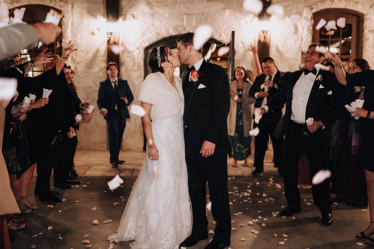 Newlyweds share romantic first dance while guests shower them with confetti in stone-walled venue.