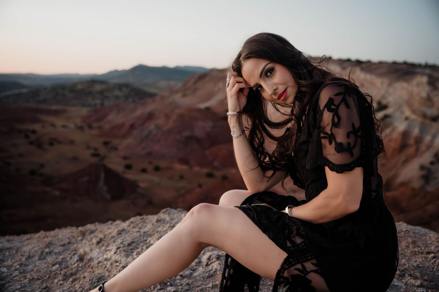 Woman relaxes on rocky terrain overlooking desert canyon at dusk.
