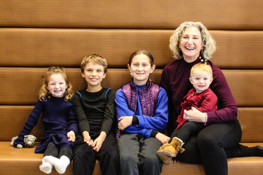 Group seated on brown bench wearing coordinated winter outfits in indoor setting.