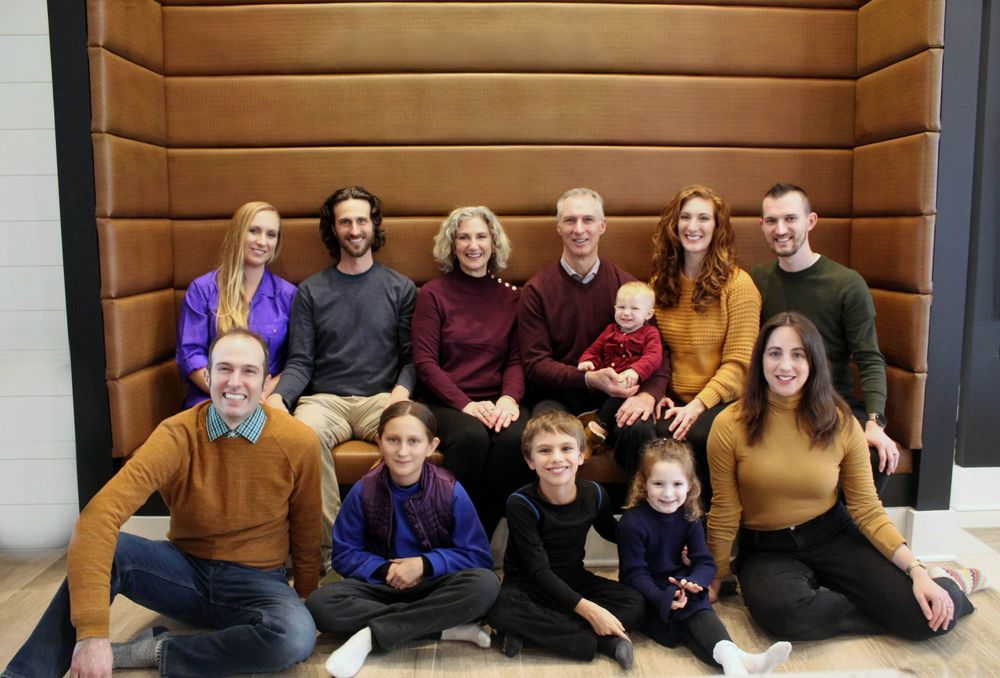 Extended family portrait gathering with multiple generations against wood panel backdrop.