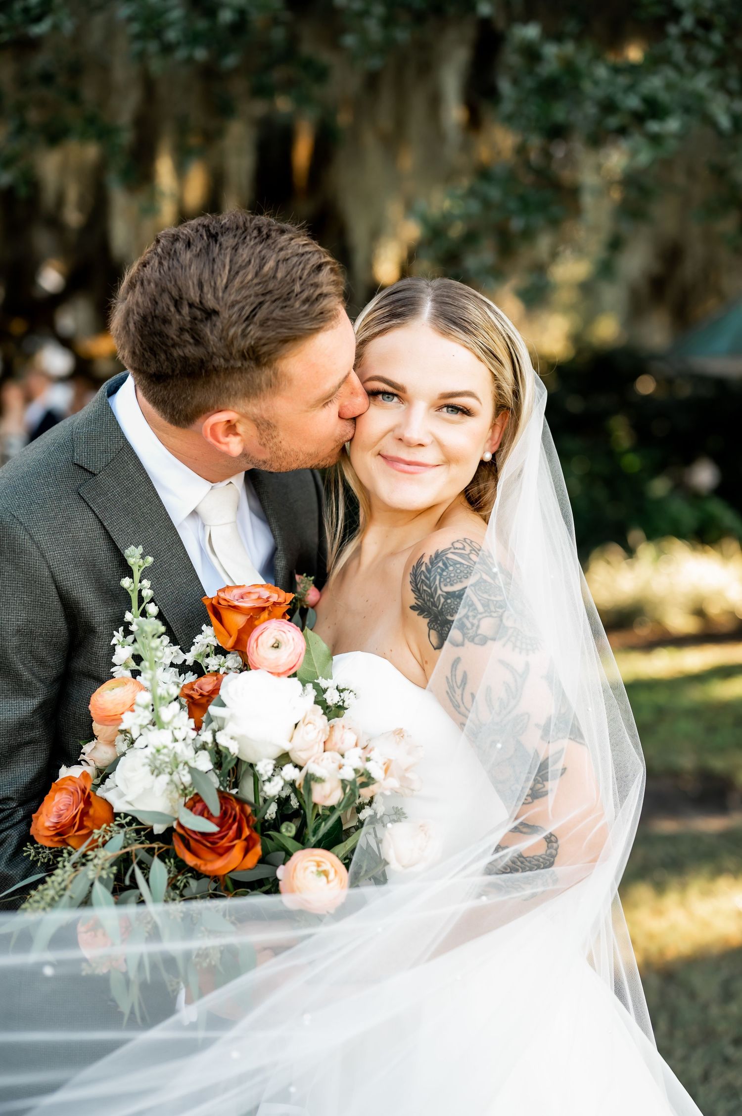 Newlyweds share intimate moment with bride holding colorful bouquet during outdoor wedding portraits.