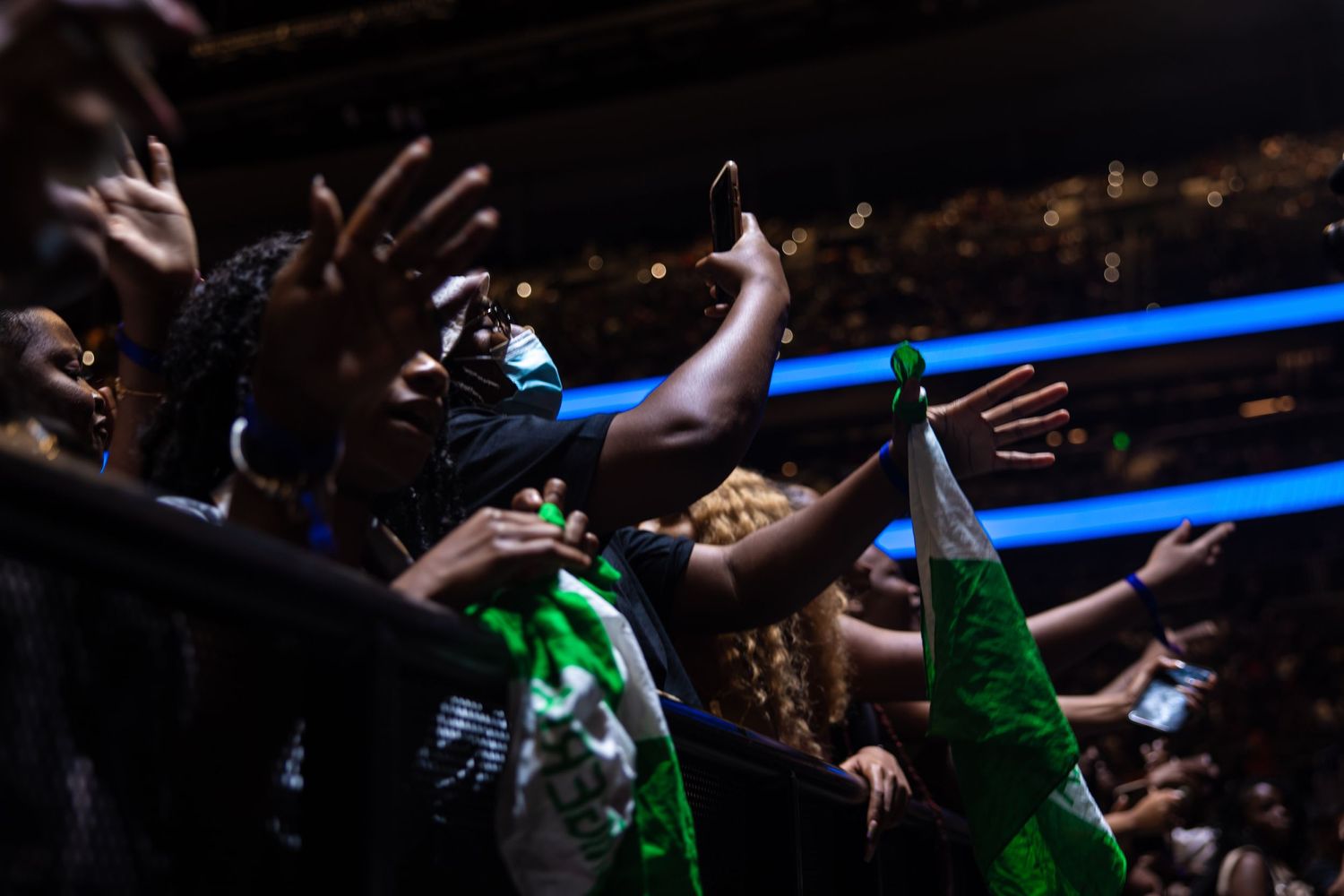 Concert audience silhouettes with raised arms against blue arena lighting.