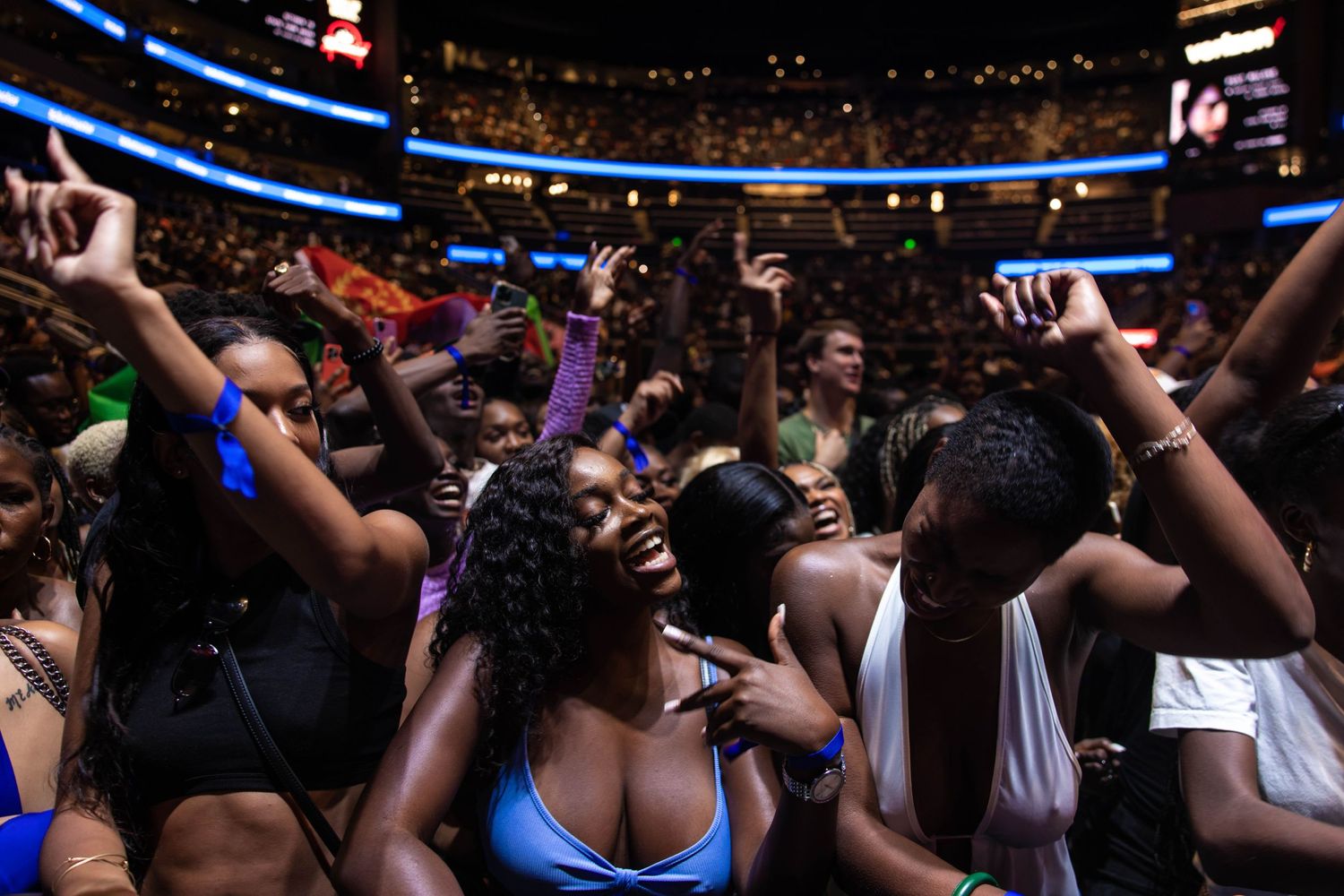 Energetic crowd at an indoor arena with hands raised during a live performance.