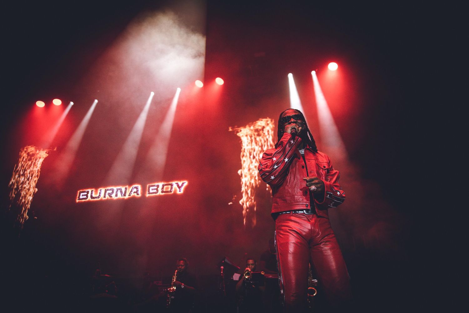 Concert production with bright spotlights and red ambient lighting creating dramatic ambiance.