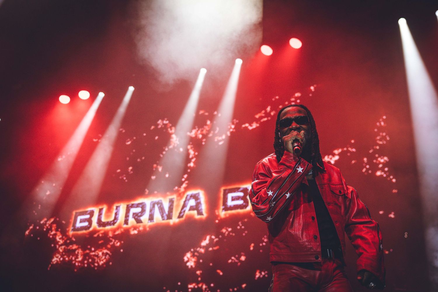 Performer on stage with 'Burna B' text display and dramatic red concert lighting.
