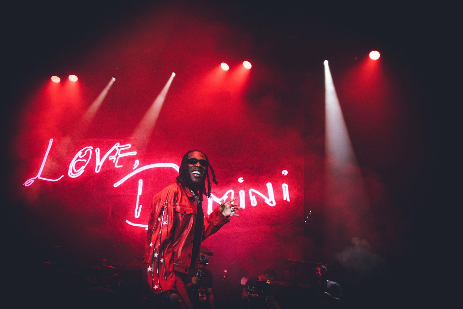 Performer on stage with red lighting and neon 'Love Damini' sign during concert performance.