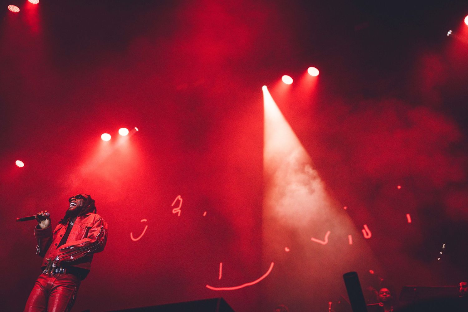 Dramatic red concert lighting illuminates performer on stage through atmospheric smoke effects.