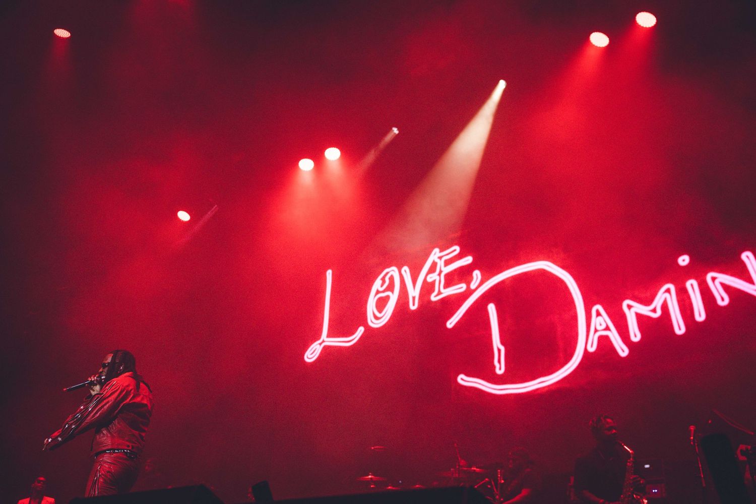 Red-lit concert stage featuring glowing 'Love Damini' neon signage against dark background.