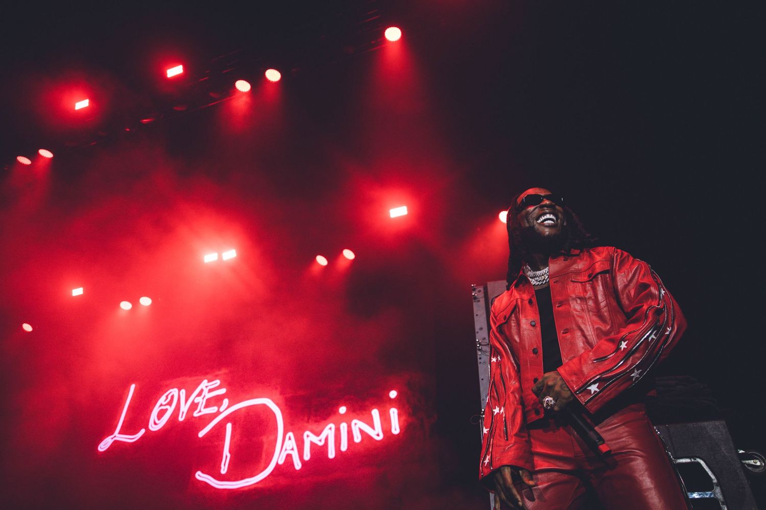 Concert stage with neon 'Love Damini' sign and dramatic red lighting effects.