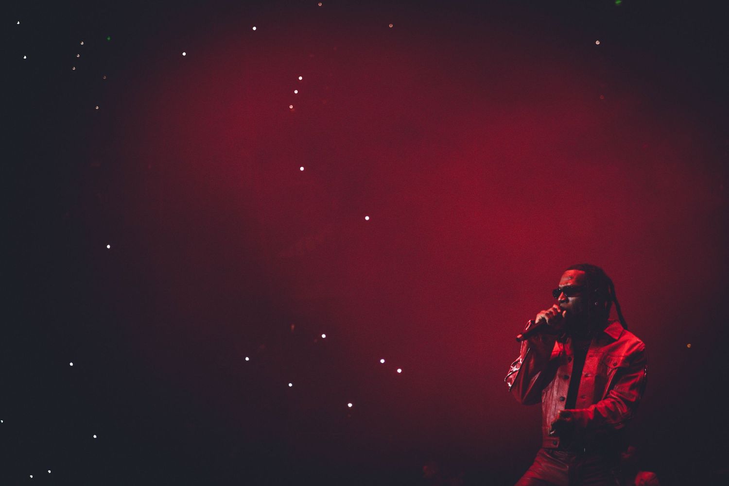 Moody concert scene with performer silhouetted against deep red lighting and starry effects.