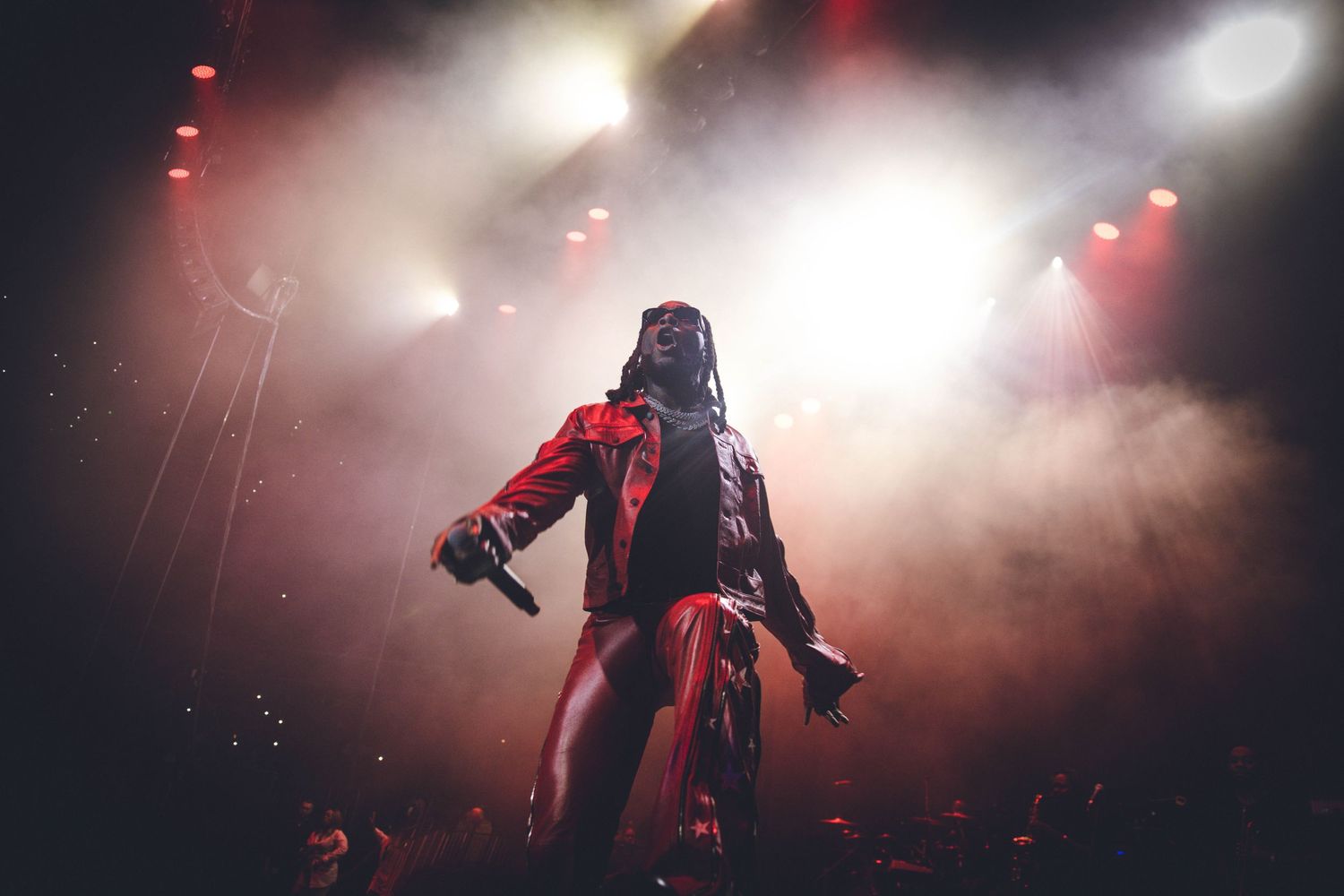 Stage performer in red outfit strikes dynamic pose amid theatrical smoke and lighting.