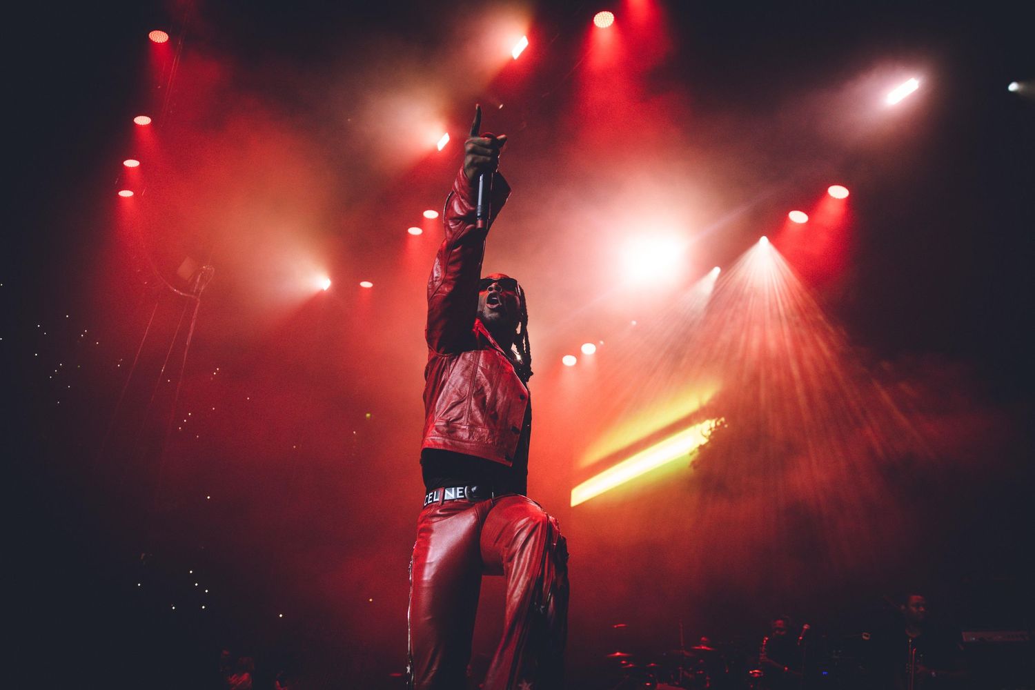 Dynamic stage performance with dramatic upward pose against red-lit smoky backdrop.