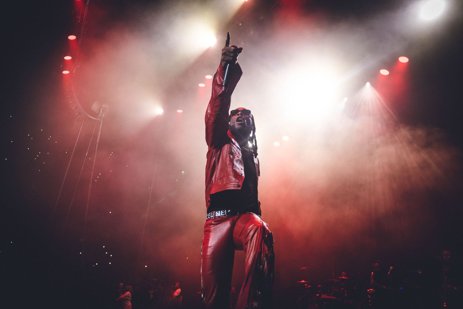 Concert performer raises arms triumphantly on stage with dramatic red and white lighting effects.