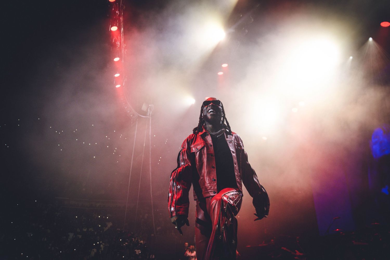 Dramatic concert performance with figure in red outfit against foggy backdrop with striking lighting.
