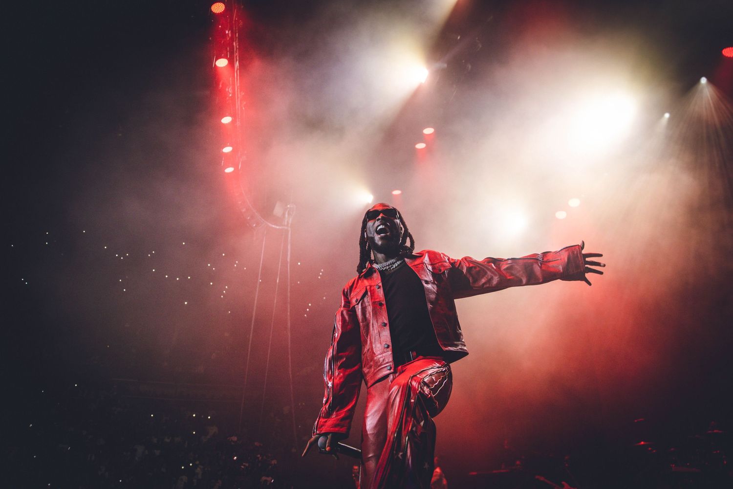 A performer in red attire poses dramatically on stage with atmospheric fog and red lighting effects.