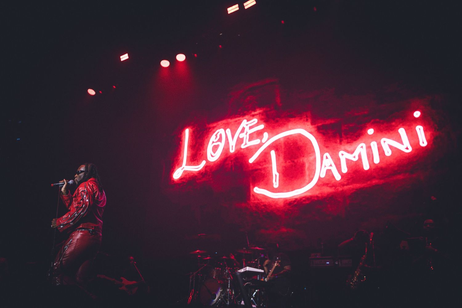 Concert performance with glowing 'Love Damini' neon sign and dramatic red stage lighting.