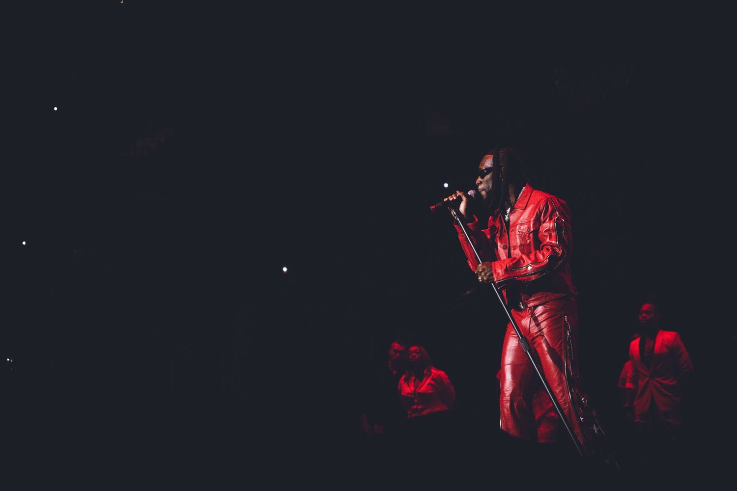Silhouetted performer in red outfit singing on dark stage with dramatic lighting.