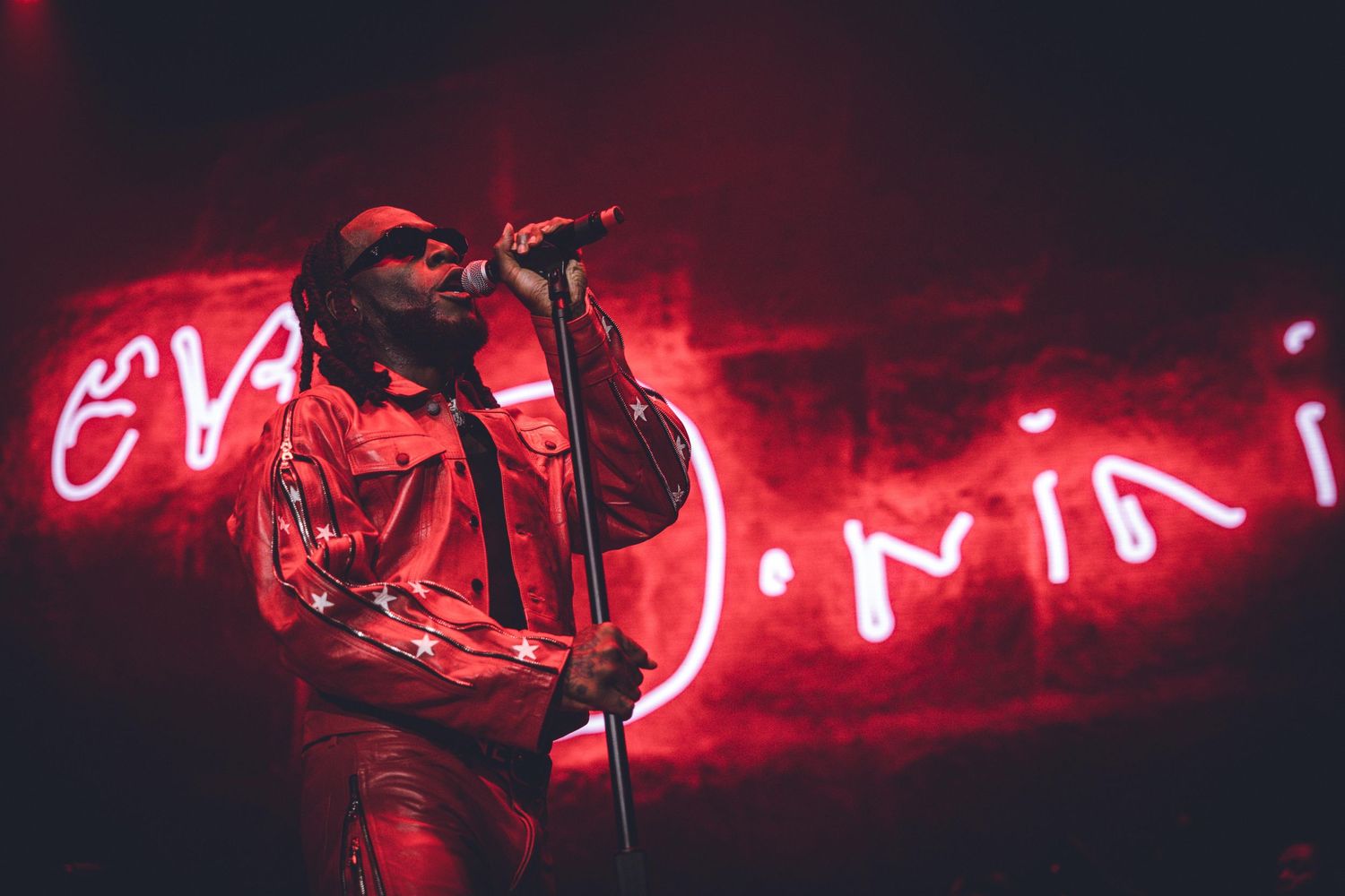 Stage performance with glowing red neon signage and dramatic concert lighting.