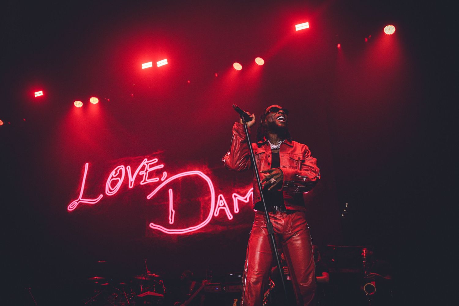 Concert stage with 'Love Dam' neon sign and red lighting creating a moody atmosphere.