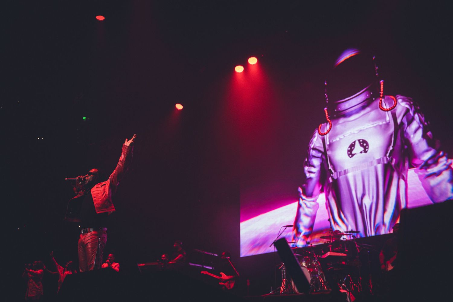 Concert performer in metallic space suit costume illuminated by red stage lights.